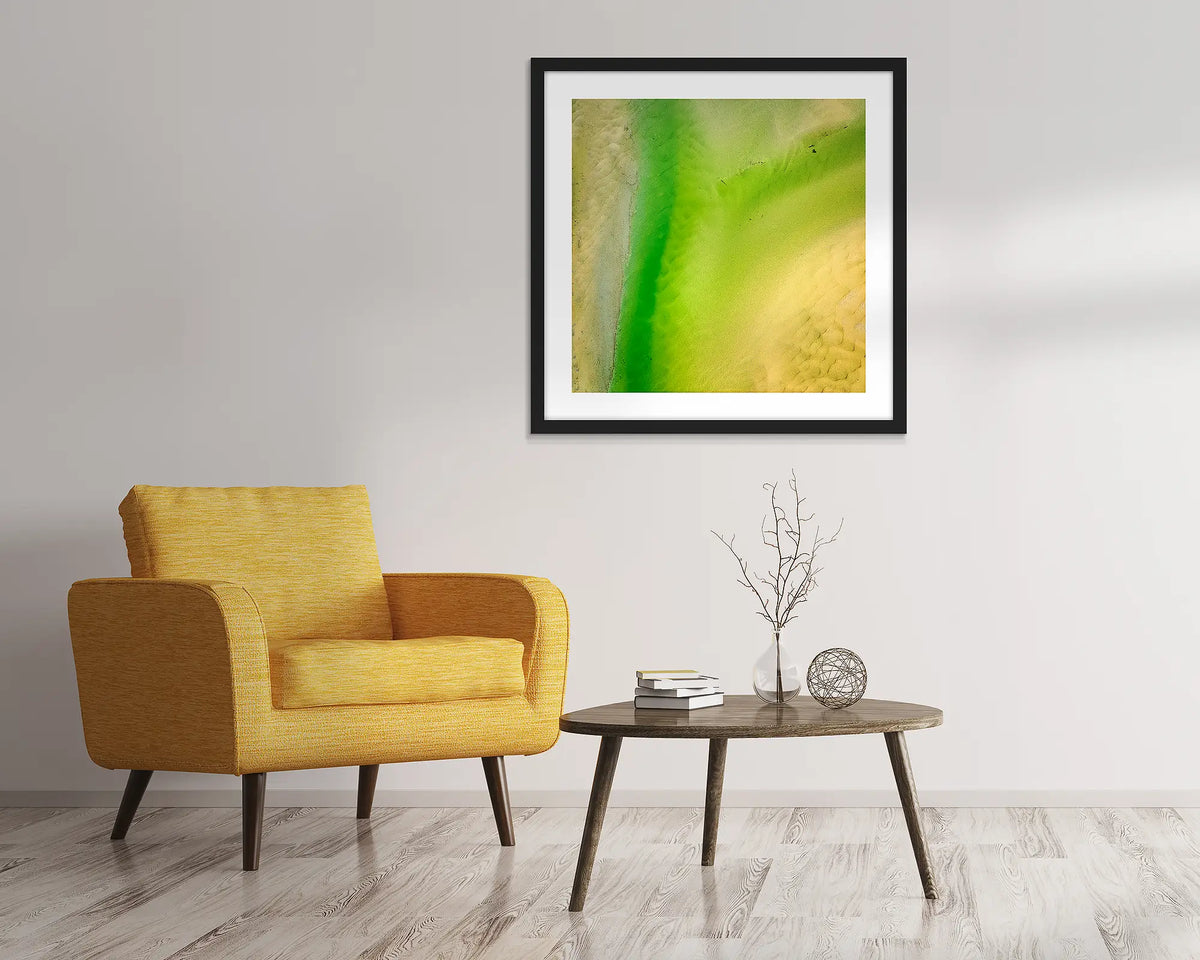 Lemon and Lime. Abstract, aerial wall art of Durras, framed in a black frame and hung above a chair.