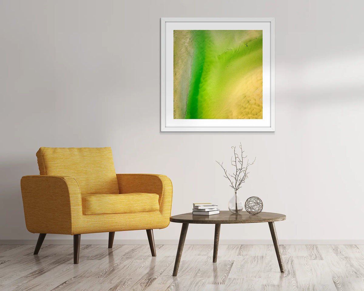 Lemon and Lime. Abstract, aerial wall art of Durras, framed in a white frame and hung above a chair.