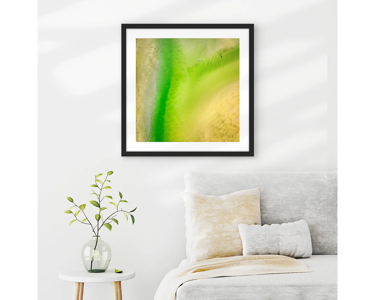 Lemon and Lime. Abstract wall art print of Durras Lake, framed in a black frame and hung above a bed. 