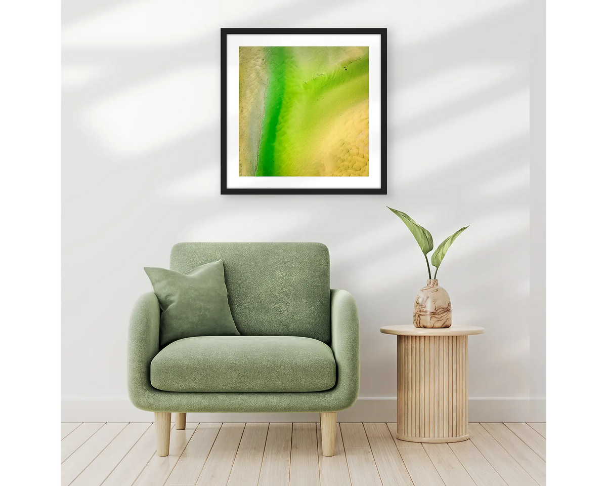 Lemon and Lime. Abstract wall art print of Durras Lake, framed in a black frame and hung above a single seat couch. 