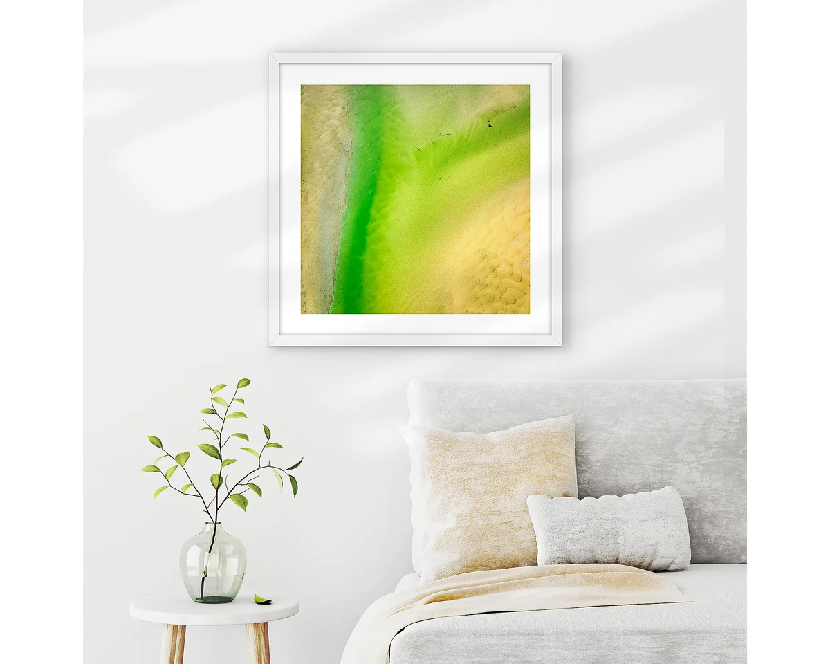 Lemon and Lime. Abstract wall art print of Durras Lake, framed in a white frame and hung above a bed. 