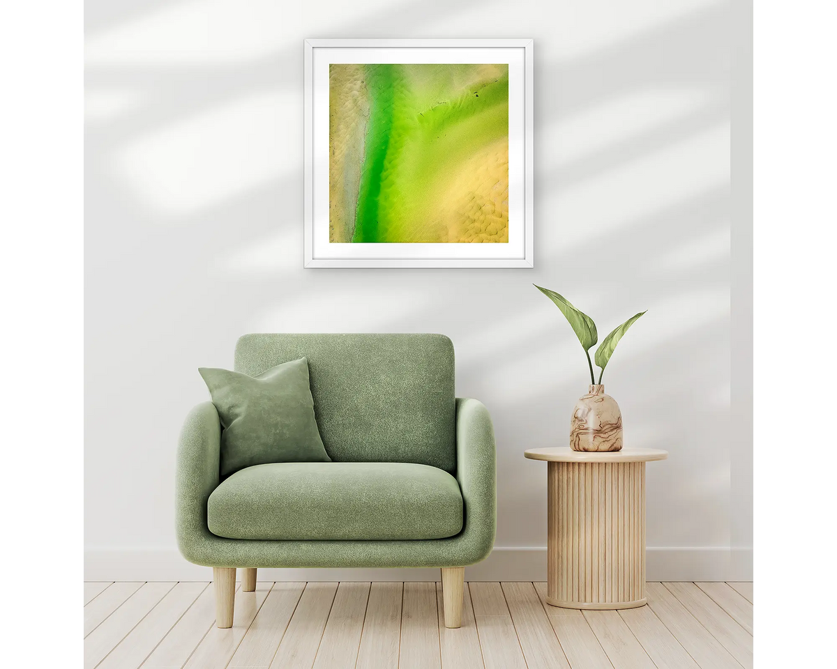 Lemon and Lime. Abstract wall art print of Durras Lake, framed in a white frame and hung above a single seat couch. 