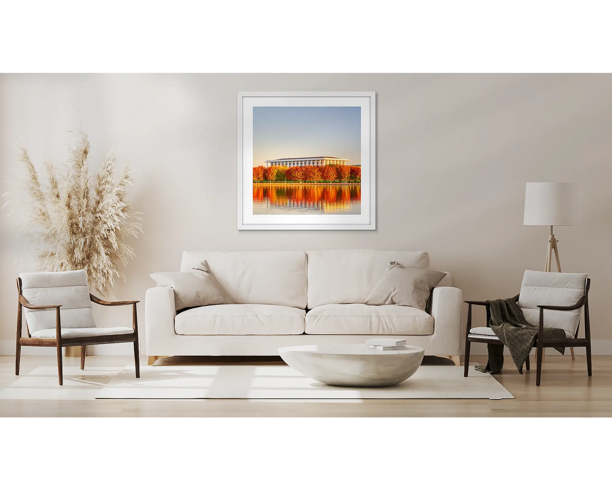 Library Reds. Wall art print with a white frame, of a sunset over autumn colours, beside the National Library of Australia, hung above a side table.