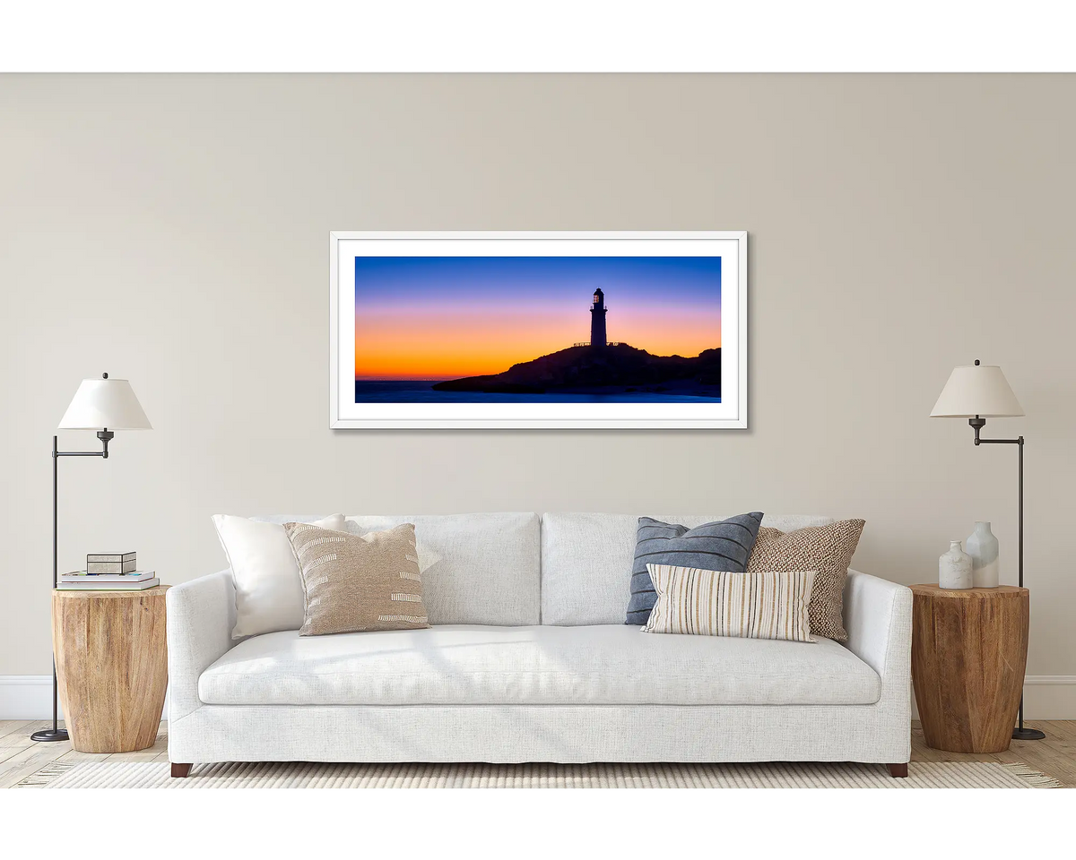 Light beyond. Wall art print of the Rottnest Island Lighthouse framed with a white frame and hung above a couch. 