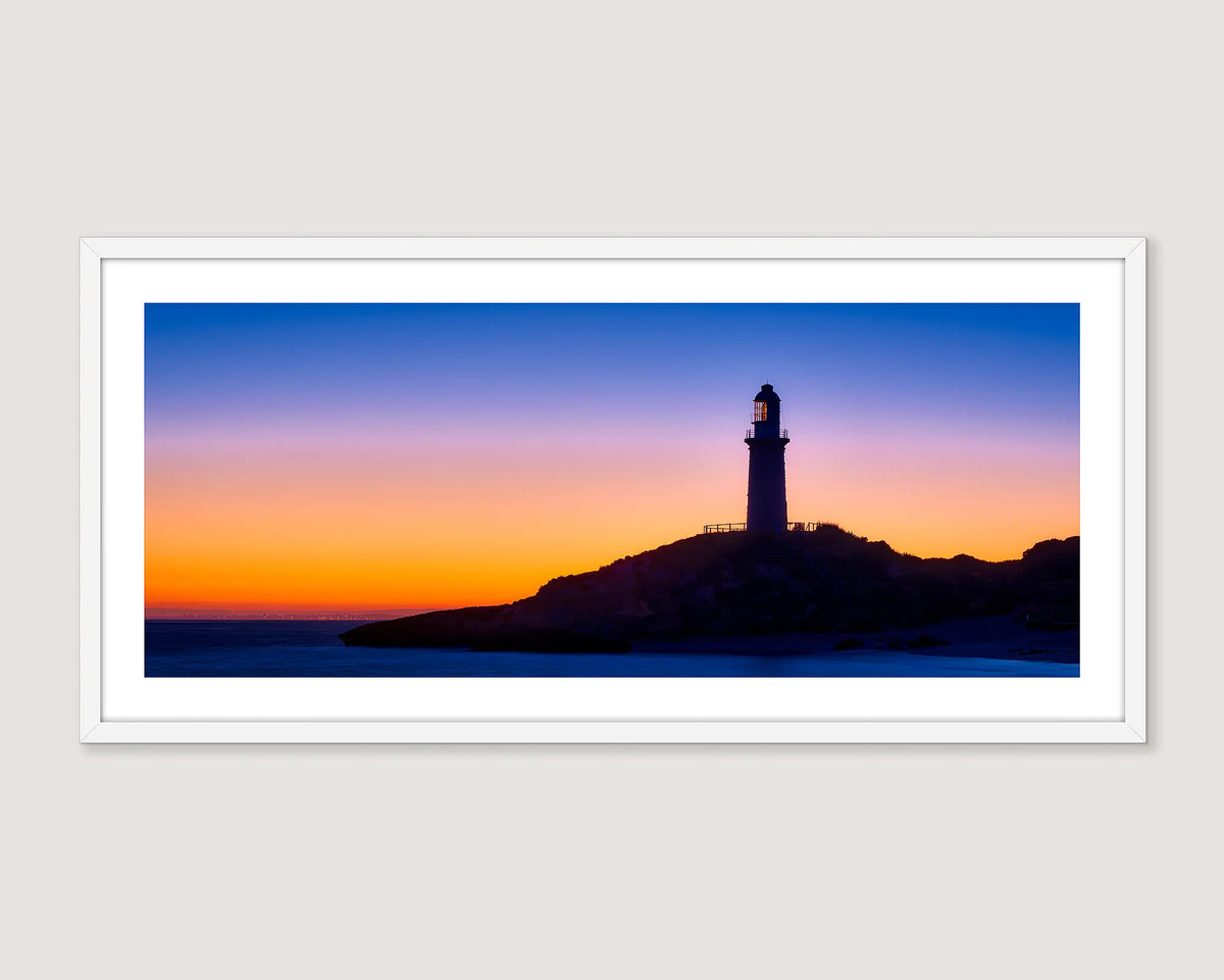 Framed wall art print of a sunrise and the Bathurst lighthouse on Rottnest Island with city lights of Perth on the horizon.