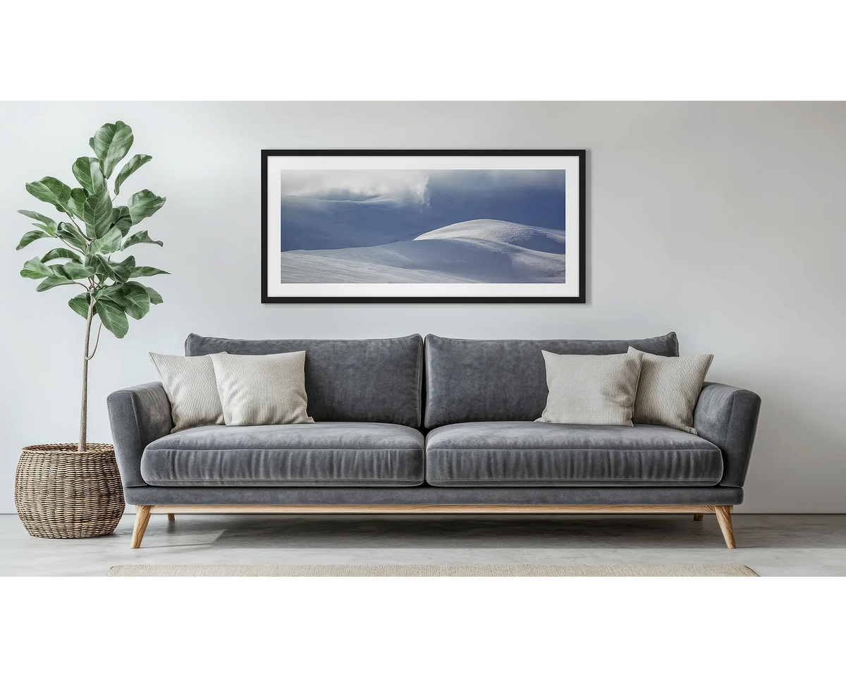 Light Show. Wall art print of light filtering through cloud, onto snow,  framed in a black frame, and hung above a couch. 