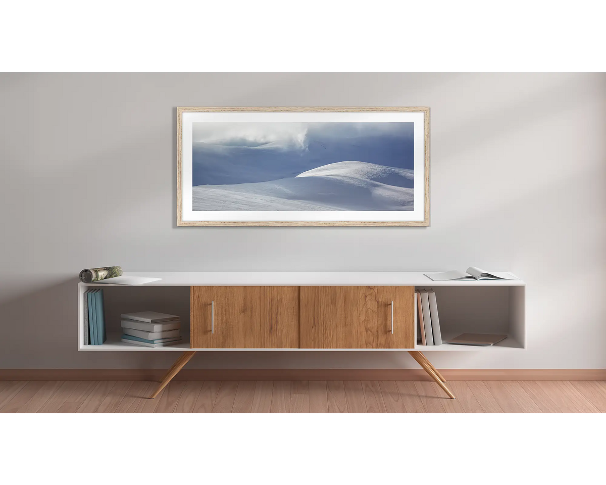 Light Show. Wall art print of light filtering through cloud, onto snow,  framed in a timber frame, and hung above a side table. 