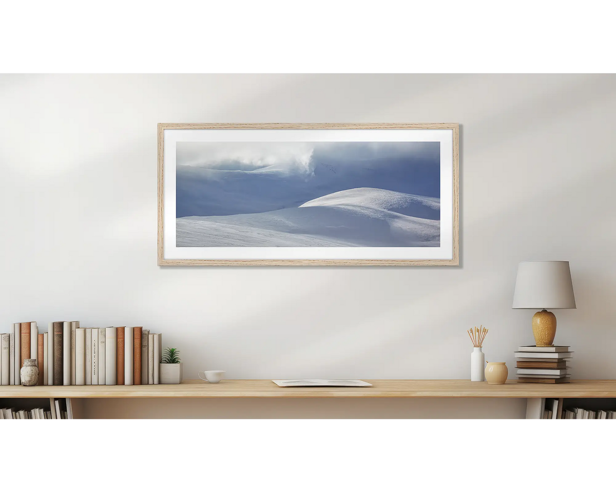 Light Show. Wall art print of light filtering through cloud, onto snow,  framed in a timber frame, and hung above a small wooden shelf. 