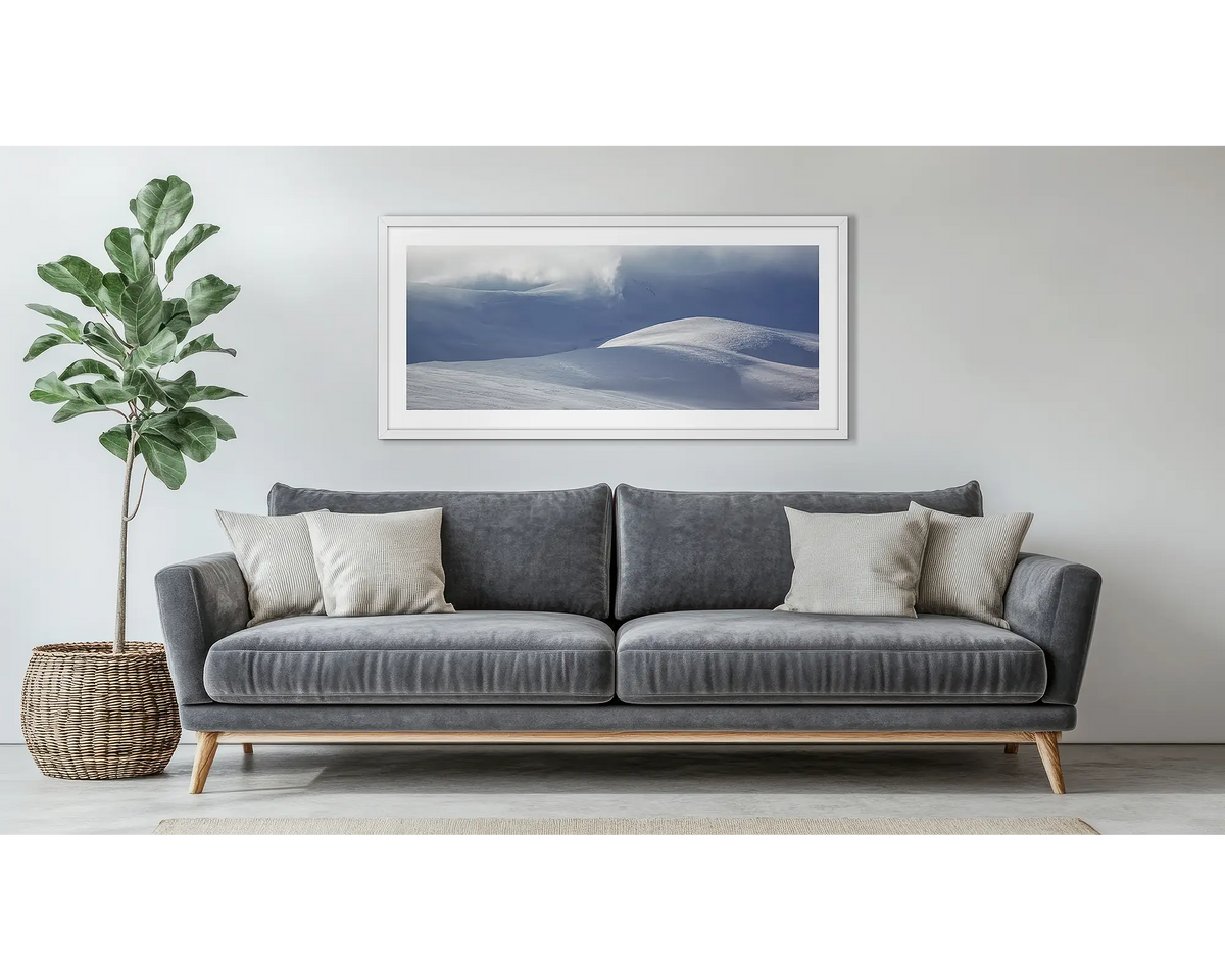 Light Show. Wall art print of light filtering through cloud, onto snow,  framed in a white frame, and hung above a couch. 