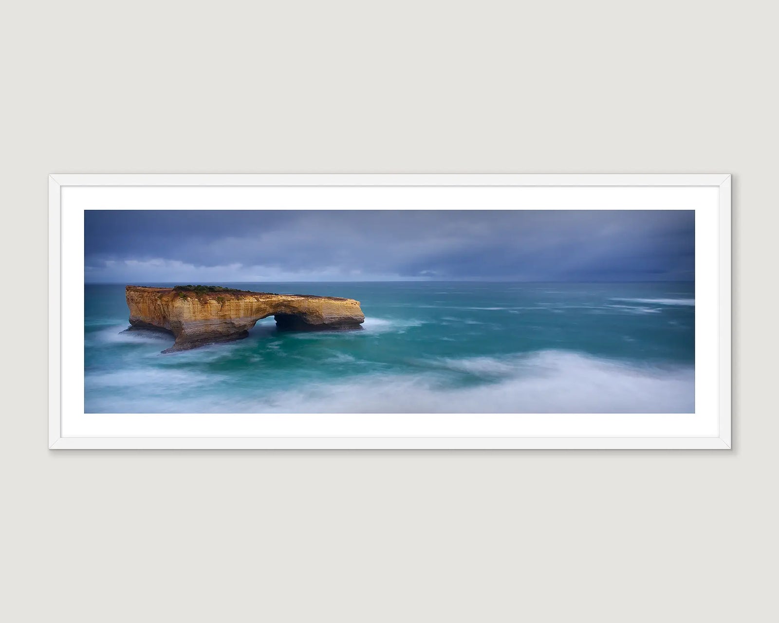 Framed photograph of a bridge rock formation in stormy seas.
