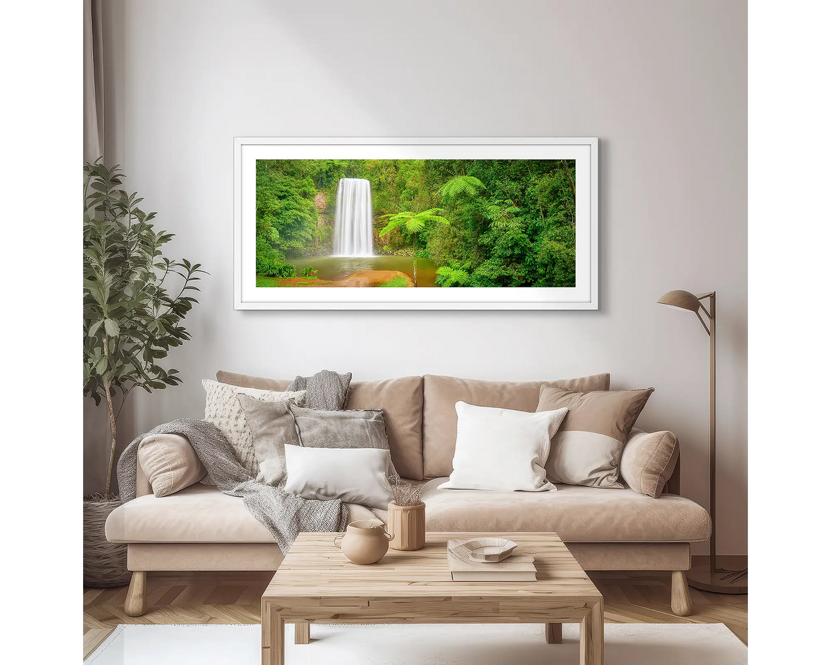 Lush. Wall art print of Milla Milla waterfall, framed with a white frame, hung in an apartment above a couch. 