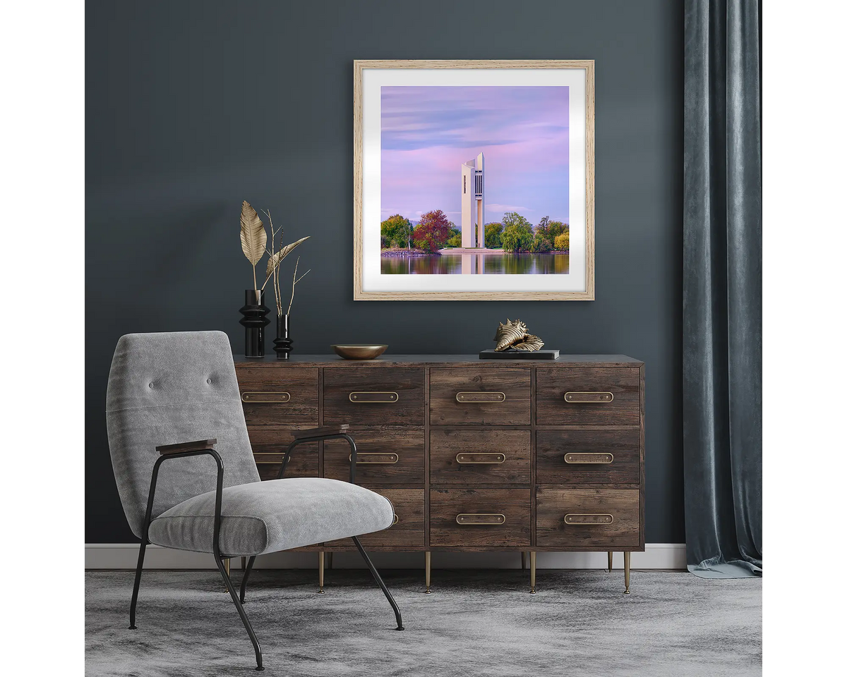 Magenta Dawn. Wall art print with timber frame of National Carillon Canberra, at sunrise, hung in a room with dark walls.