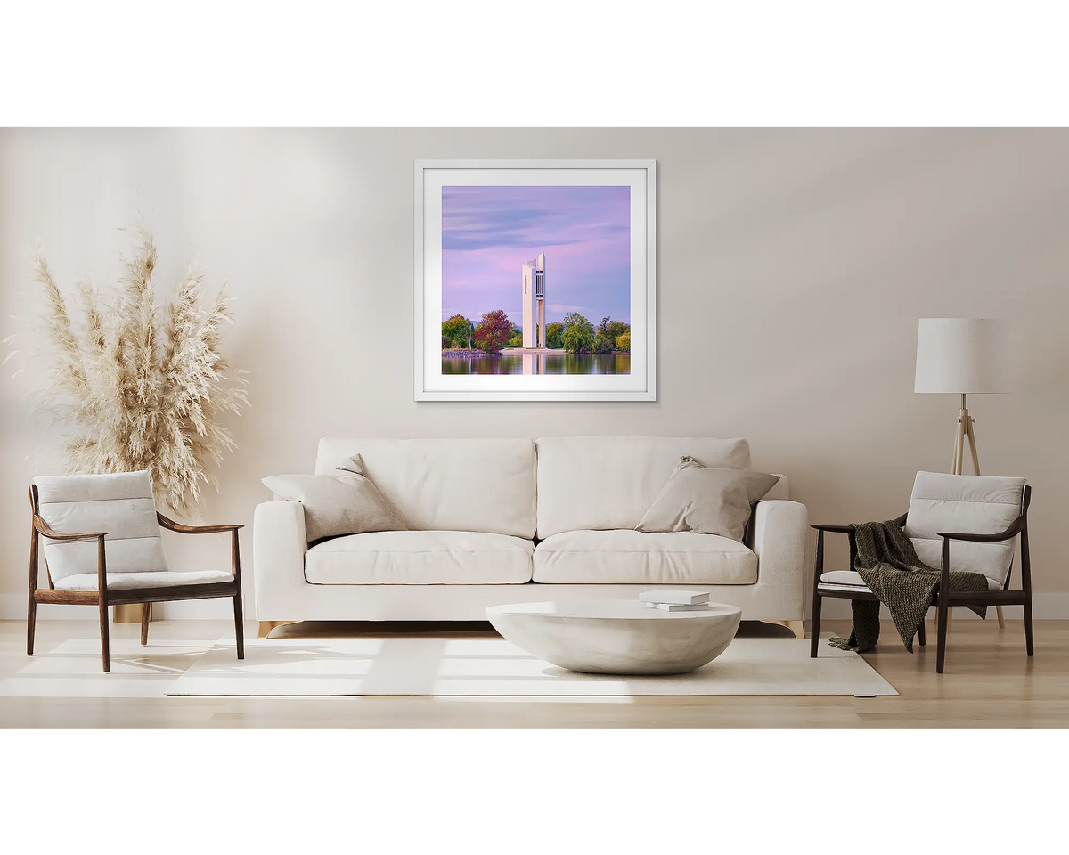 Magenta Dawn. Wall art print with a white frame, of a sunrise over the National Carillon, Canberra, hung above a couch.