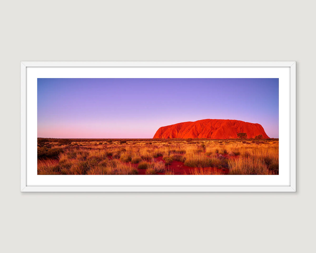 Framed artwork of Uluru with a purple sky at sunset.