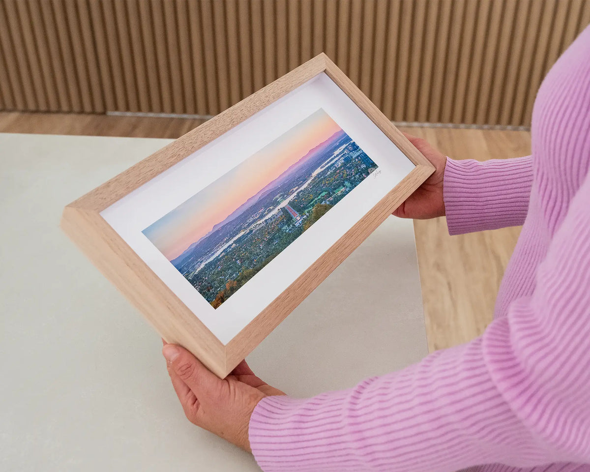 Marion's View. Small print with timber frame of sunrise over Canberra from Mount Ainslie, held in hands.