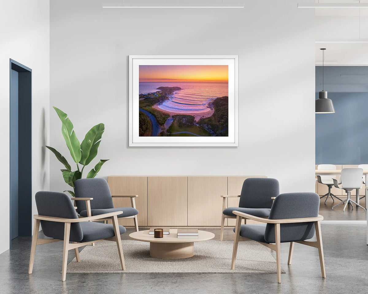 McKenzies Glow.  Wall art print of a sunrise over McKenzie&#39;s Beach, with a white frame, hung on the wall of a waiting area.