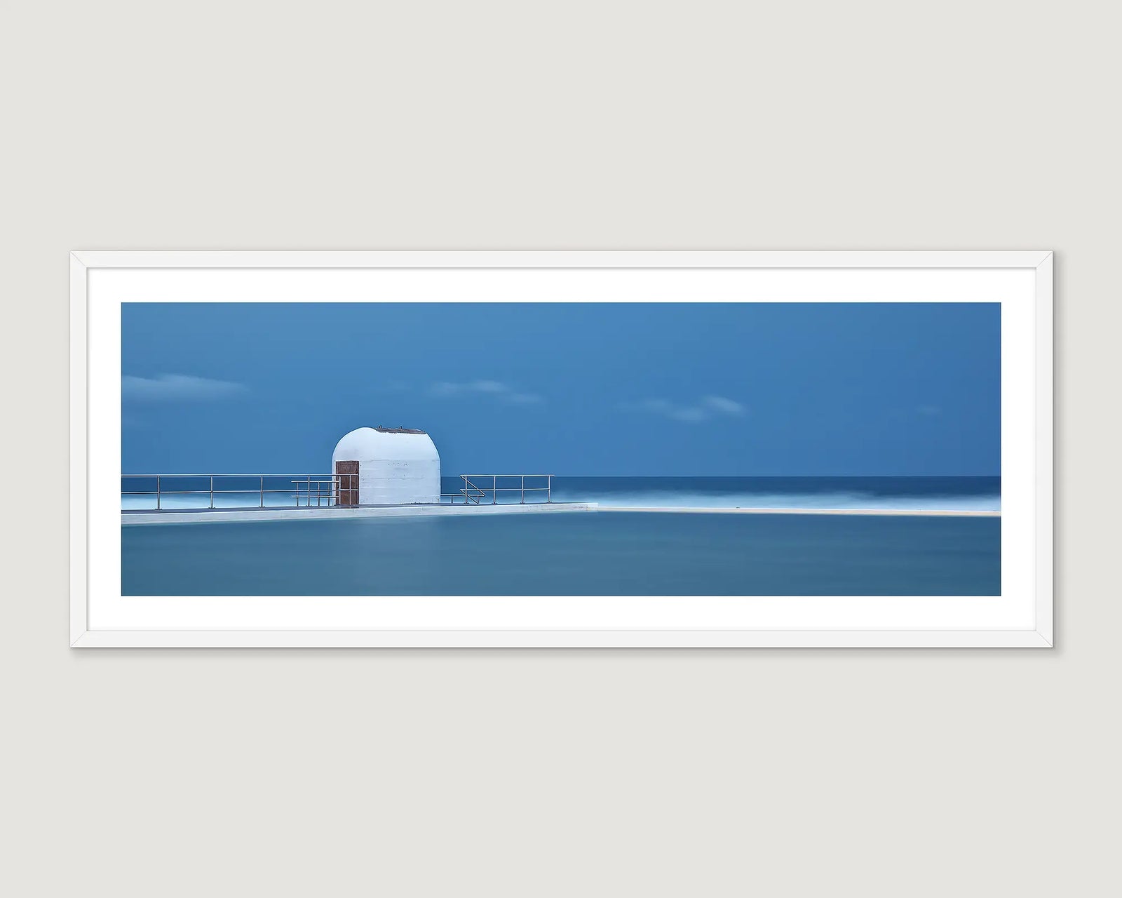 Framed photograph of an ocean bath and white building against a blue stormy sky.