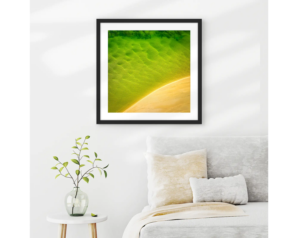 Mosaic. Aerial view of Durras Lake, wall art print in a black frame hung in a neutral bedroom. 