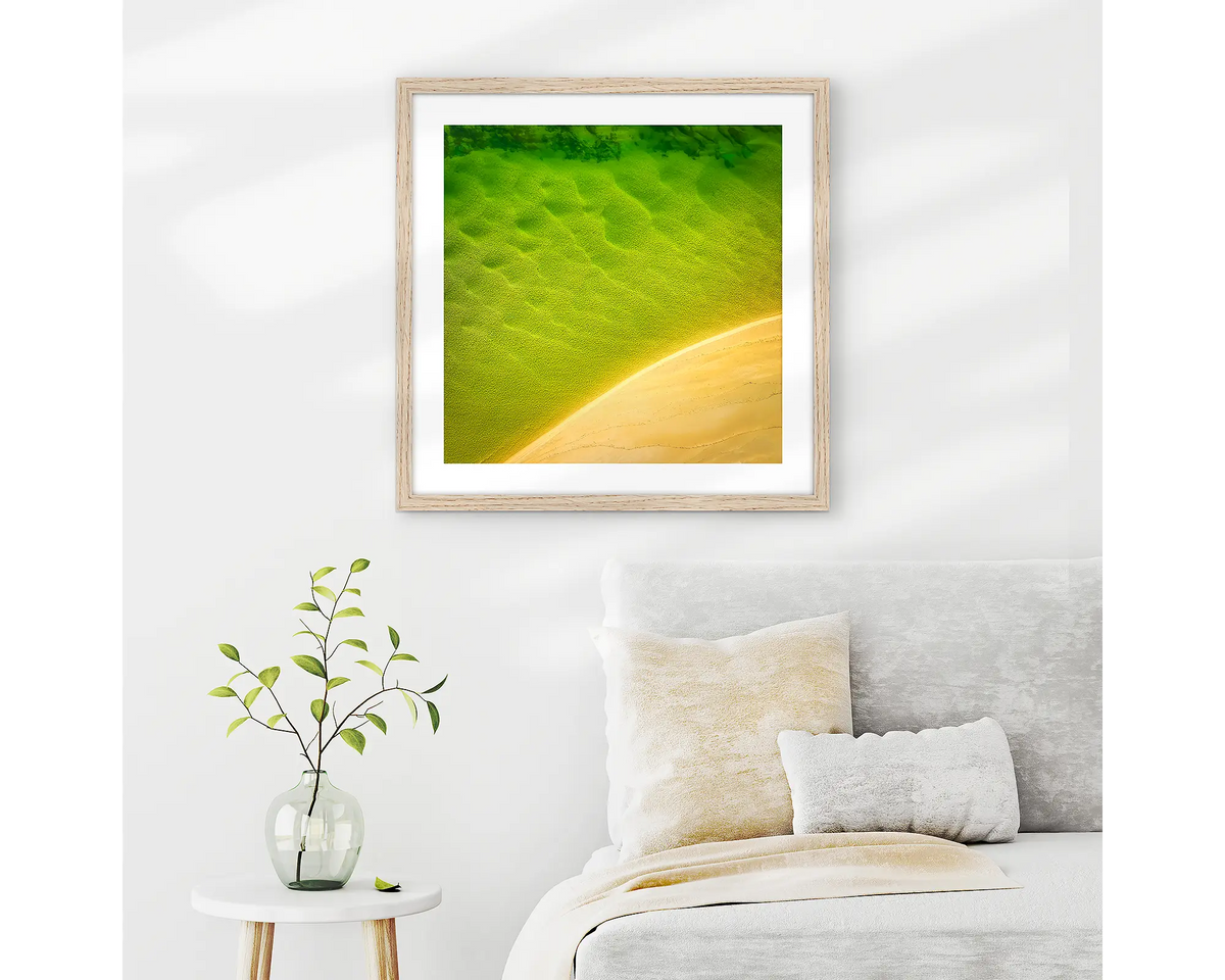 Mosaic. Aerial view of Durras Lake, wall art print in a timber frame hung in a neutral bedroom. 