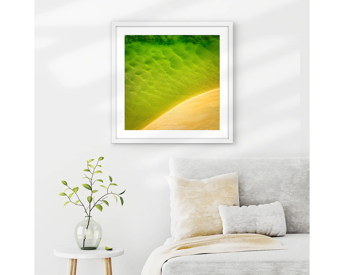 Mosaic. Aerial view of Durras Lake, wall art print in a white frame hung in a neutral bedroom. 
