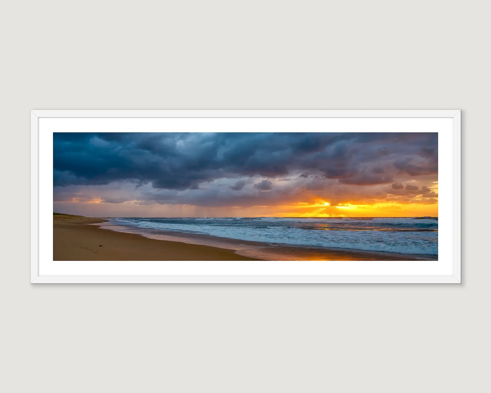 Framed landscape photograph of an ocean and sand and a stormy golden sunrise.
