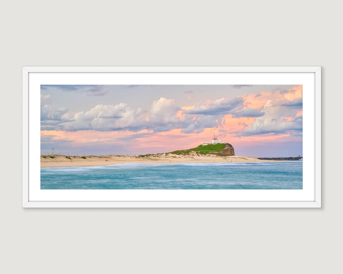 Framed landscape photograph of an ocean and sand and a pastel sunrise.