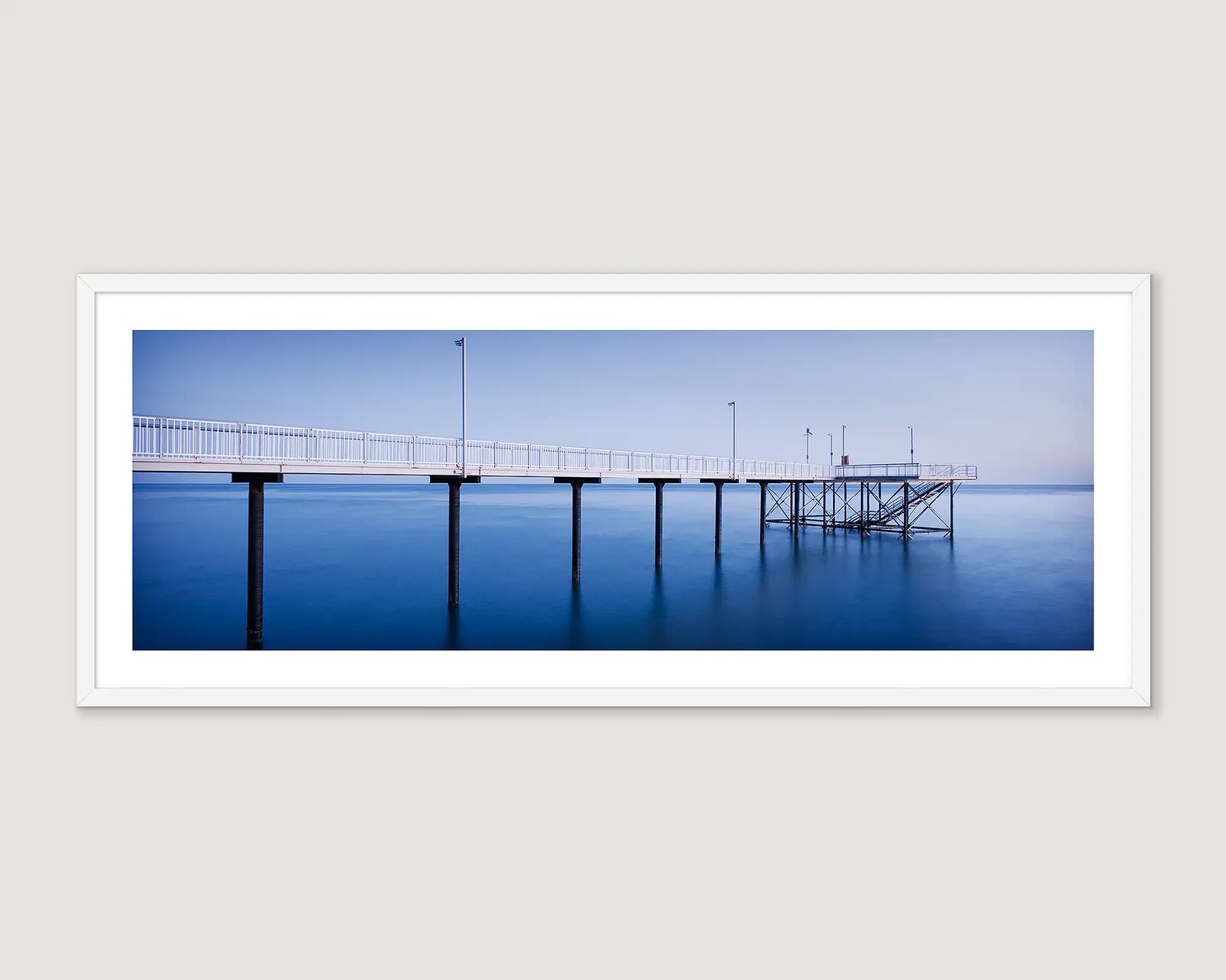 Framed landscape photograph of a jetty over the ocean in blue colours.