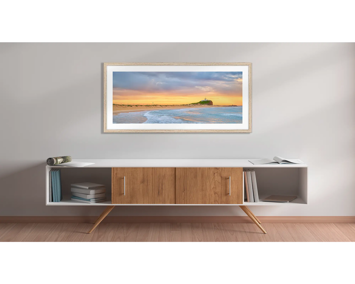 Nobby&#39;s Gold. Wall art print with a timber frame, of a golden sunrise over Nobby&#39;s beach, Newcastle, hung above a side table. 