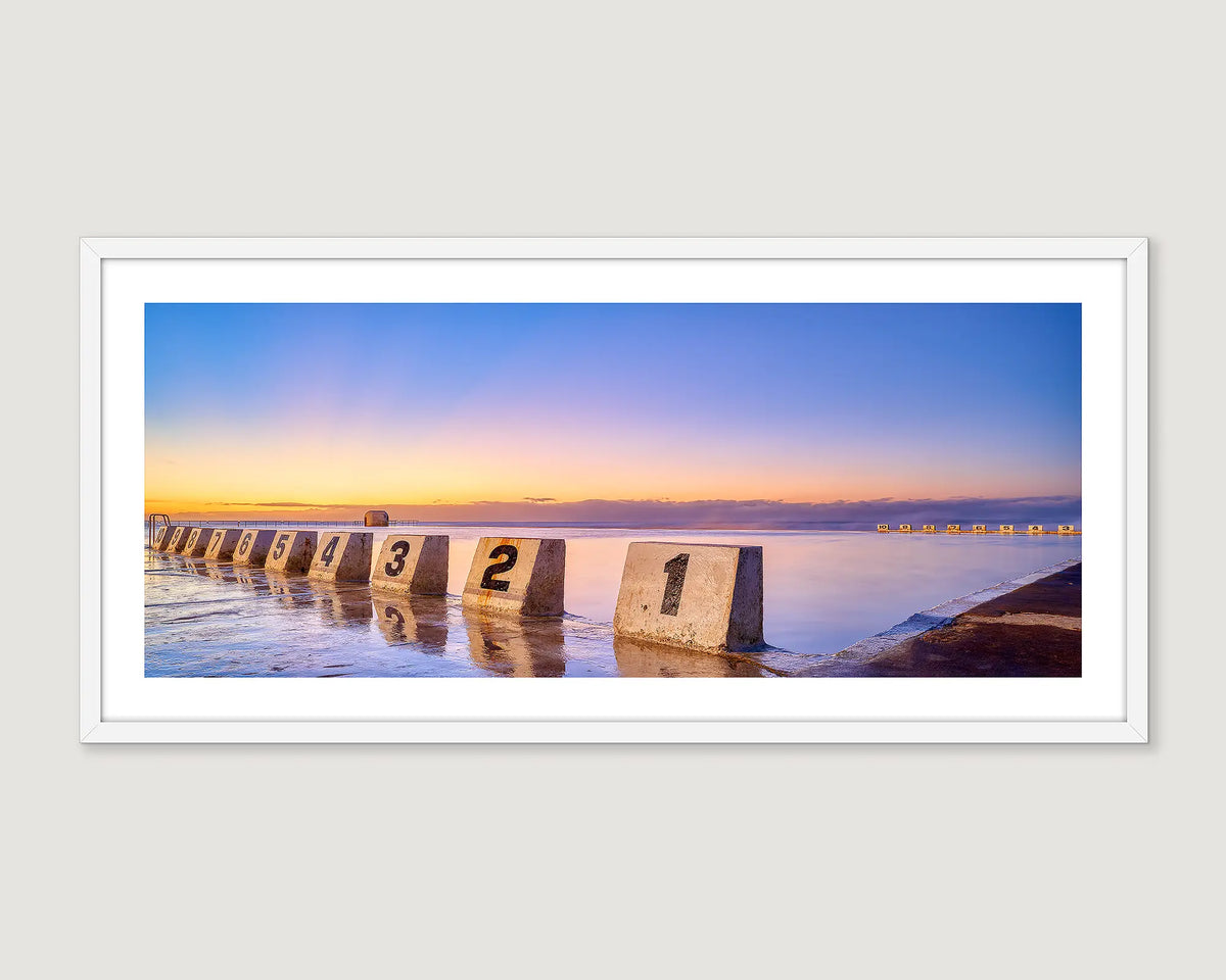 Framed coastal wall art print of a gold sunrise reflecting in the ocean water at Merewether Baths in Newcastle. 