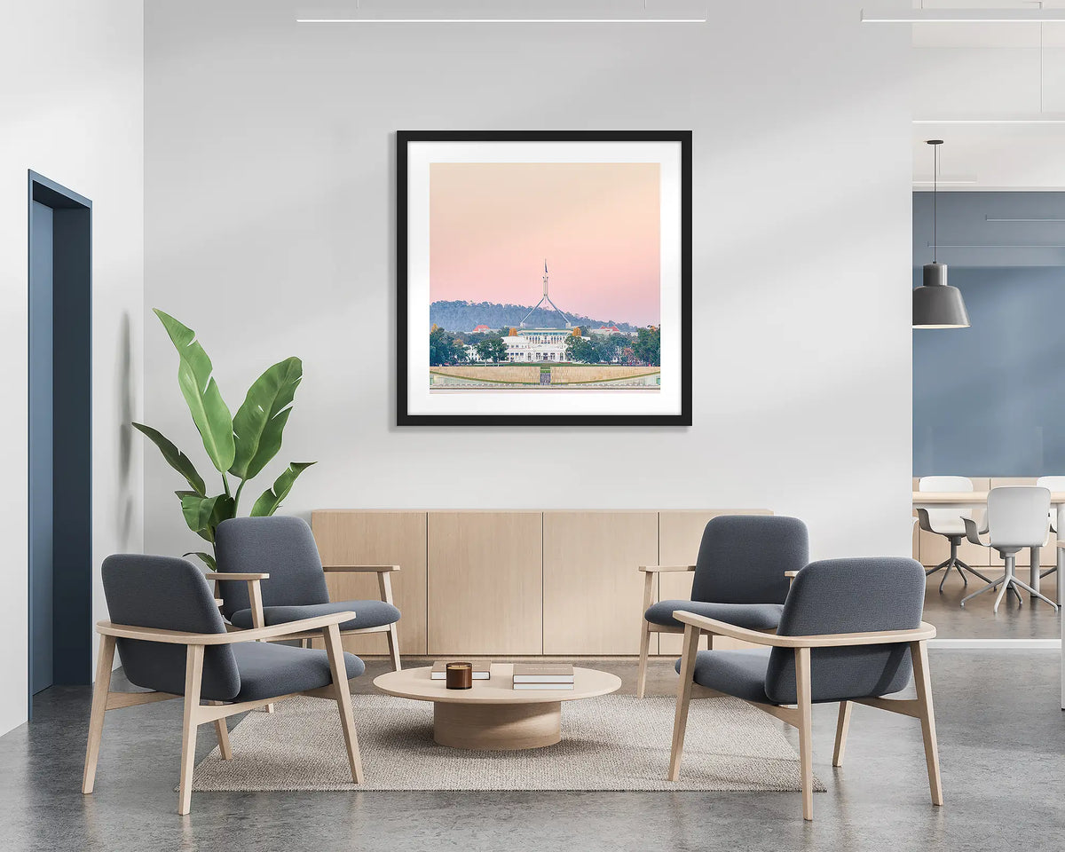 Old and New. Framed wall art print of Parliament House, Canberra, with a pink sunrise, with a black frame in a bright office lobby. 