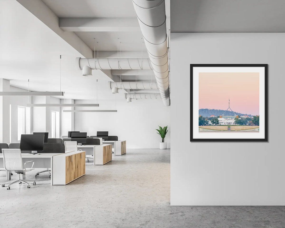 Old and New. Framed wall art print of Parliament House, Canberra, with a pink sunrise, with a black frame in a modern, open office.