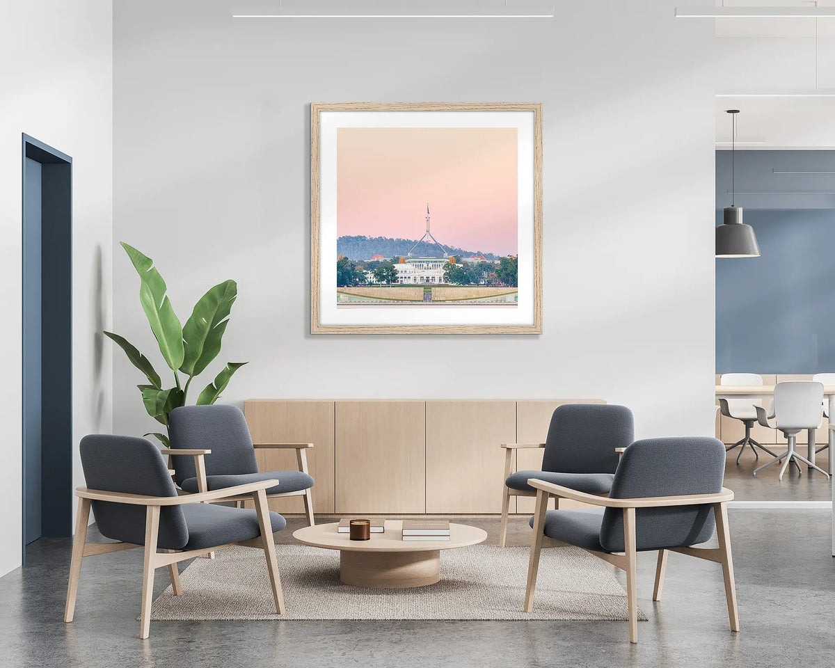 Old and New. Framed wall art print of Parliament House, Canberra, with a pink sunrise, with a timber frame in a bright office lobby. 