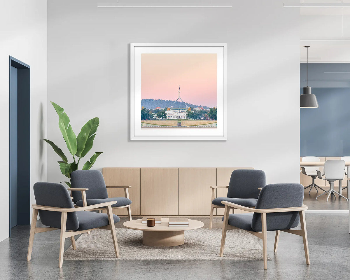Old and New. Framed wall art print of Parliament House, Canberra, with a pink sunrise, with a white frame in a bright office lobby. 