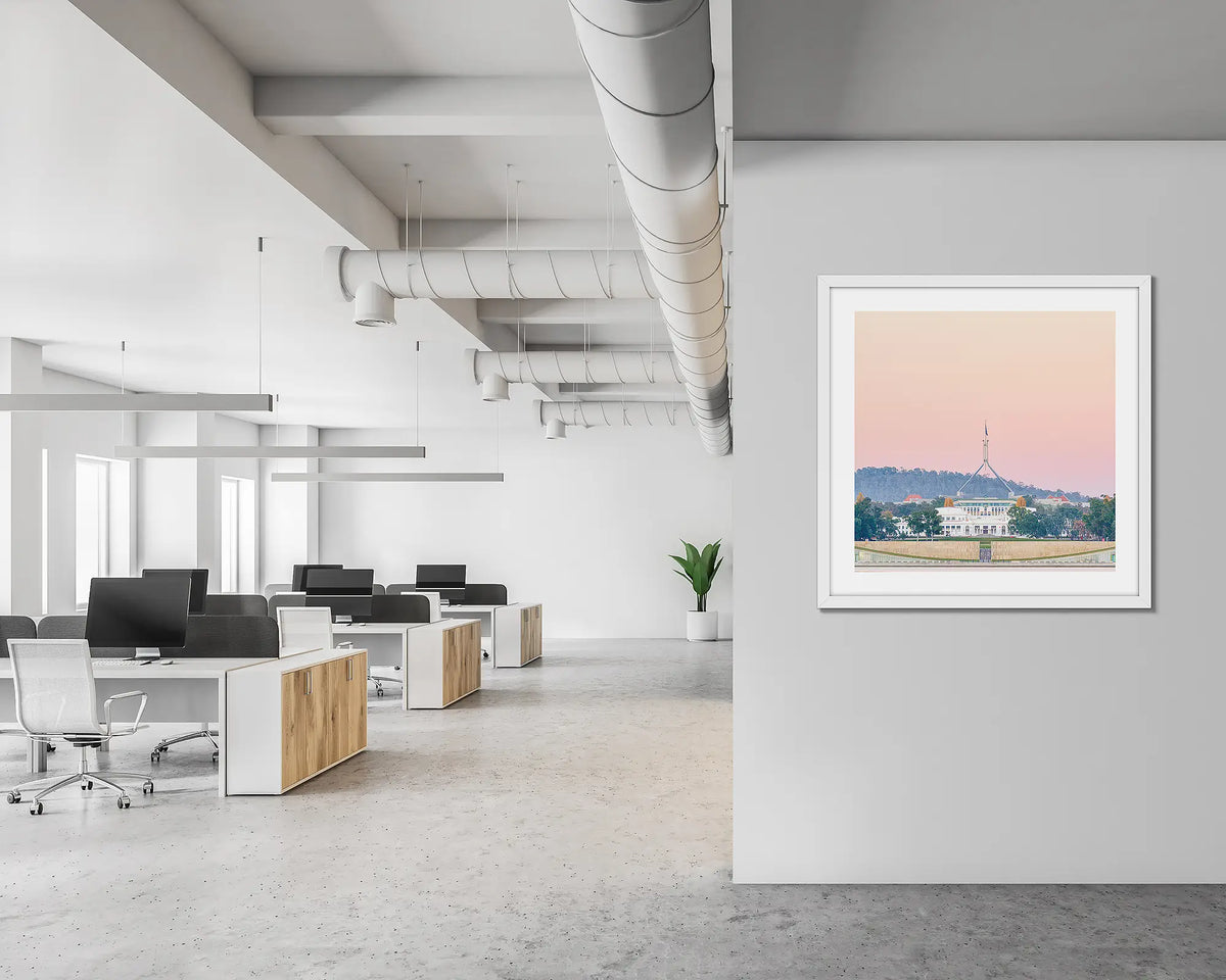 Old and New. Framed wall art print of Parliament House, Canberra, with a pink sunrise, with a white frame in a modern, open office.