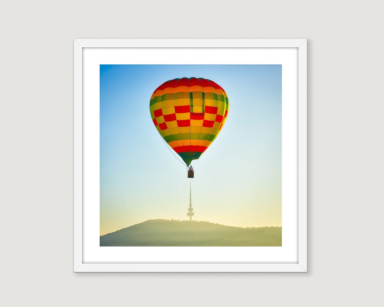 Framed photograph of a hot air balloon above a tower on a mountain.