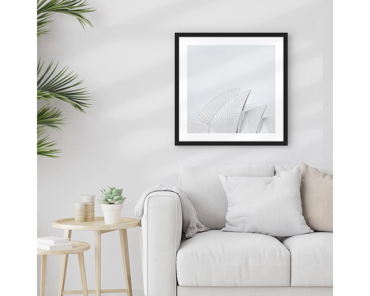 Opera House Curves. Square wall art print featuring sails of the Sydney Opera House, with a black frame, hung above a couch. 
