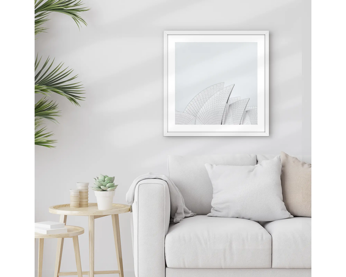 Opera House Curves. Square wall art print featuring sails of the Sydney Opera House, with a white frame, hung above a couch. 