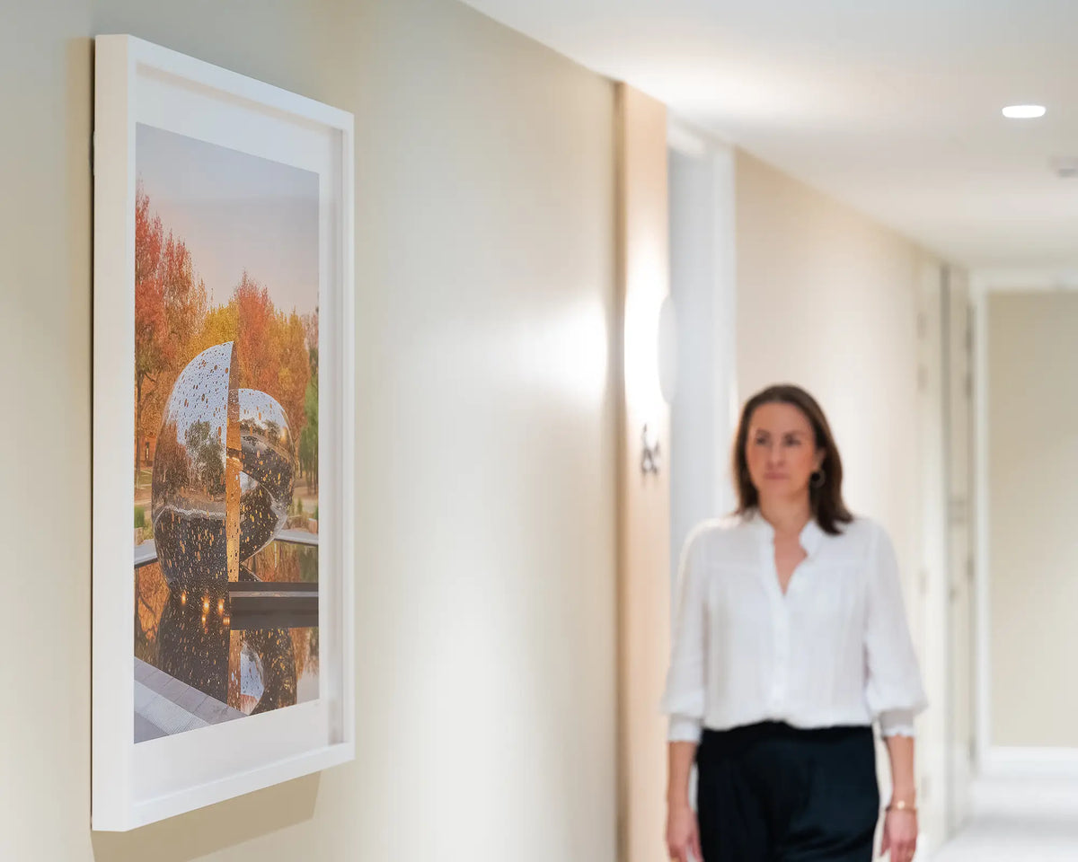 Orange Cocoon. Lindy Lee Ouroboros sculpture, National Gallery of Australia, with white frame, hung in apartment building with person walking beside.