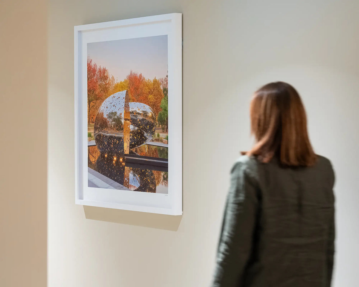 Orange Cocoon. Lindy Lee Ouroboros sculpture, National Gallery of Australia, with white frame, hung on wall with person walking toward.