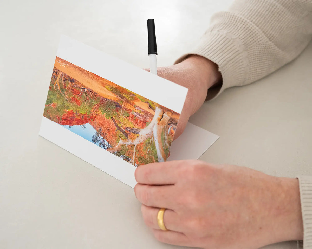 Ormiston Sanctuary greeting card of sunrise at Ormiston Gorge, with person writing a message with black pen.