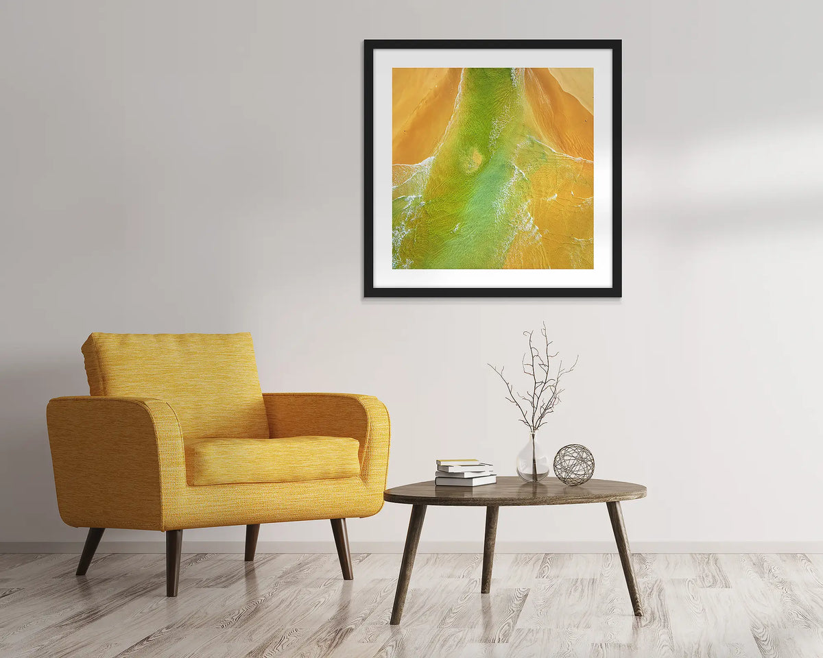Outflow. Abstract, aerial wall art of Durras, framed in a black frame and hung above a chair. 