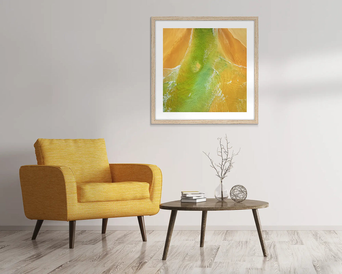 Outflow. Abstract, aerial wall art of Durras, framed in a Tasmanian Oak frame and hung above a chair. 
