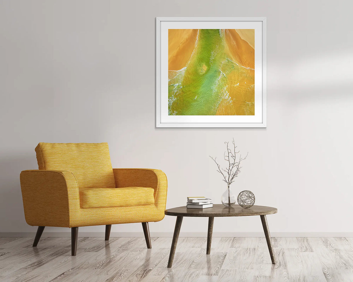 Outflow. Abstract, aerial wall art of Durras, framed in a white frame and hung above a chair. 
