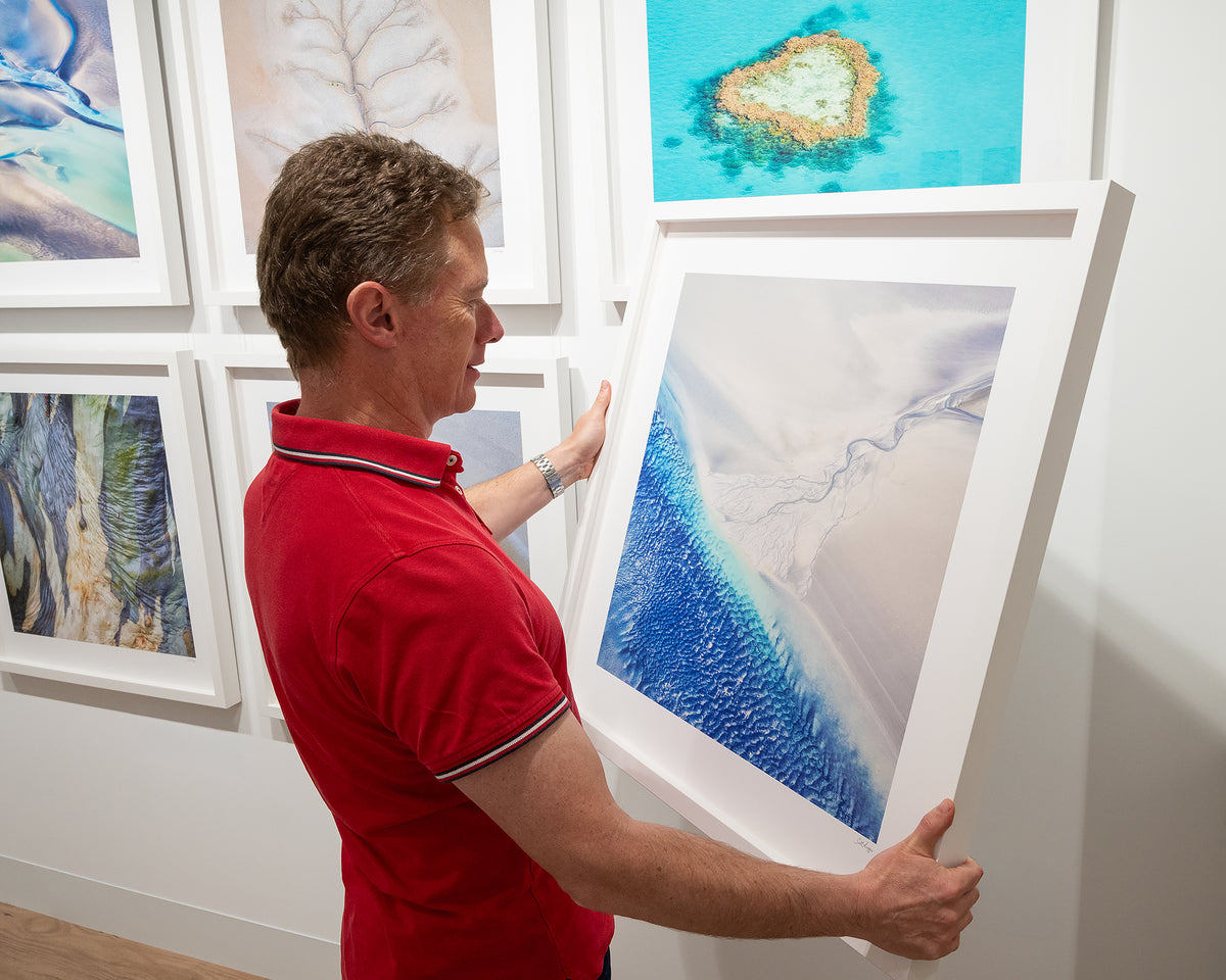 Outlet. Aerial landscape photography print with white frame in hands ready to hang on gallery wall.