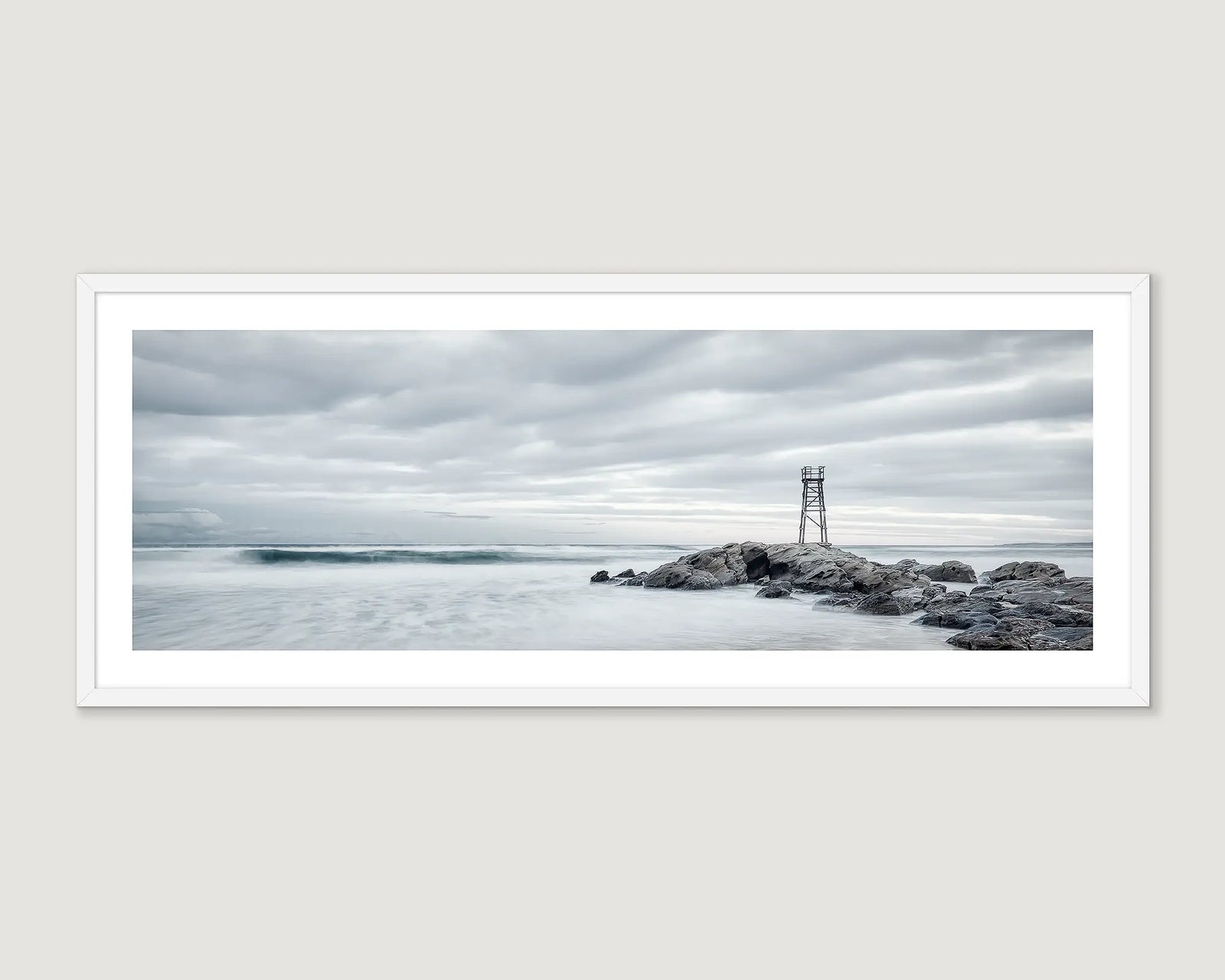 Framed photograph of the ocean with rocks and clouds.