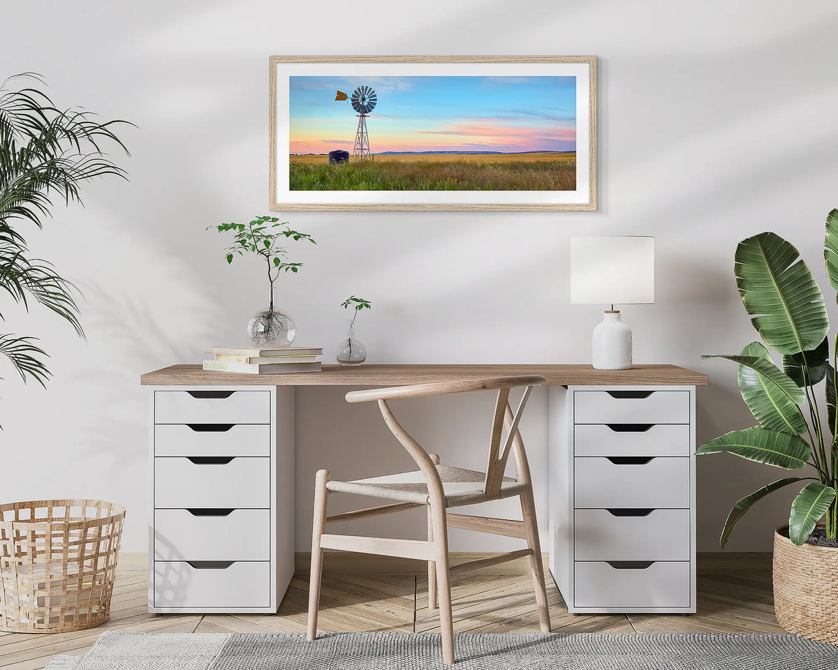 Painted Morning. Wall art print of a windmill on a farm, with a colourful sunrise, with a timber frame hung above a small desk. 