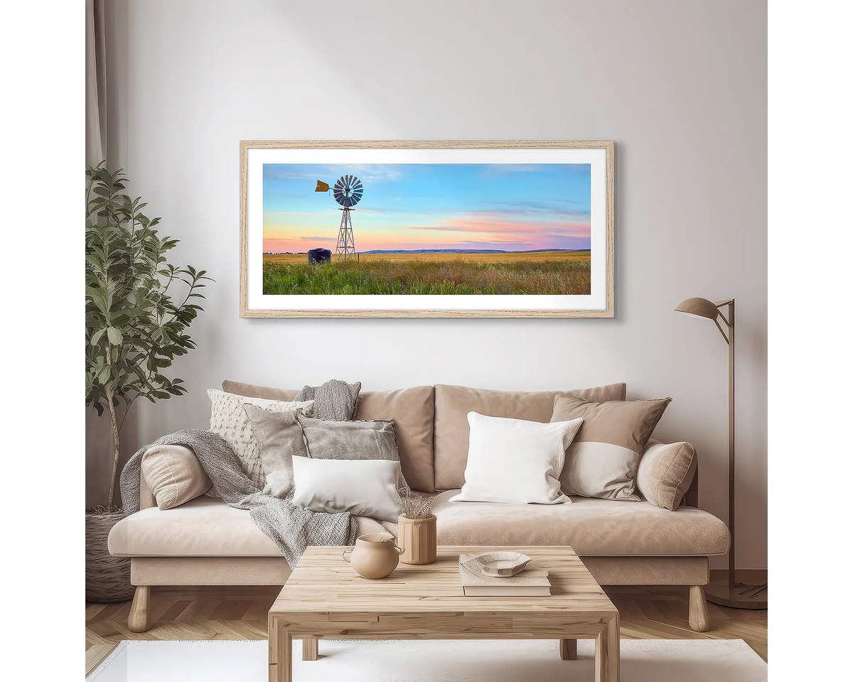 Painted Morning. Wall art print of a windmill on a farm, with a colourful sunrise, with a timber frame hung in an apartment living room. 