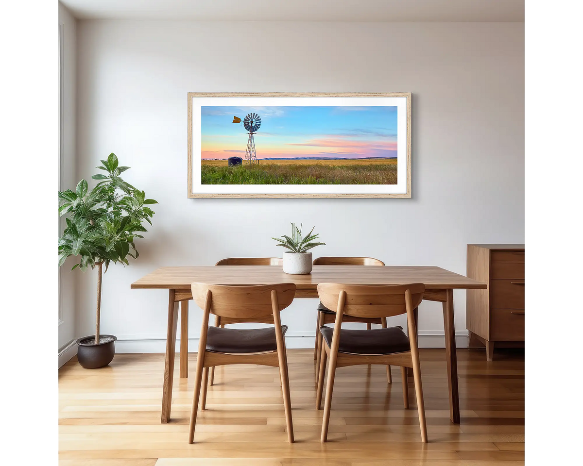 Painted Morning. Wall art print of a windmill on a farm, with a colourful sunrise, with a timber frame hung in a dining area. 