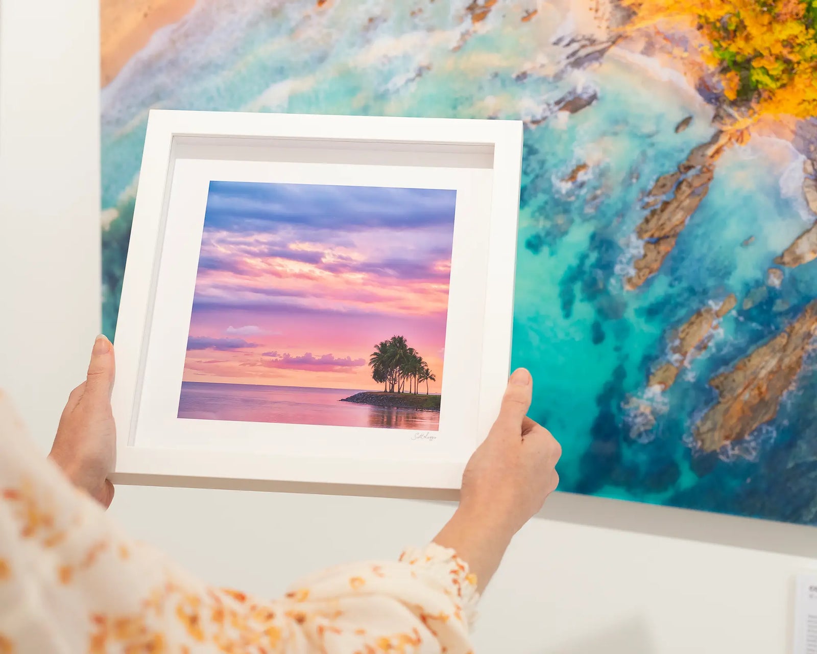 Framed photograph of palm trees and the ocean with a cloudy colourful sunset.