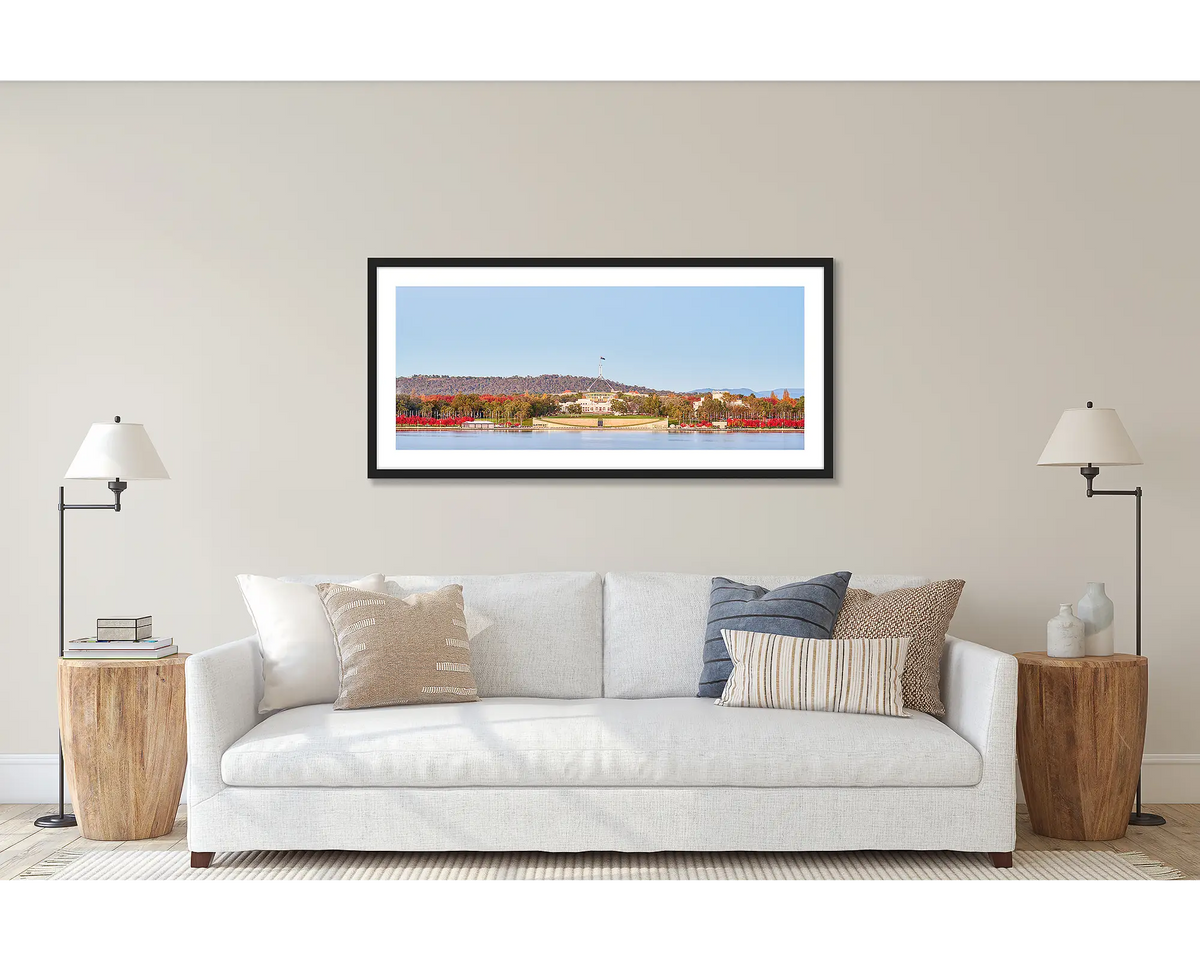 Parliamentary Reds. Wall art print of old and new Parliament House, framed in a black frame and hung above a couch. 